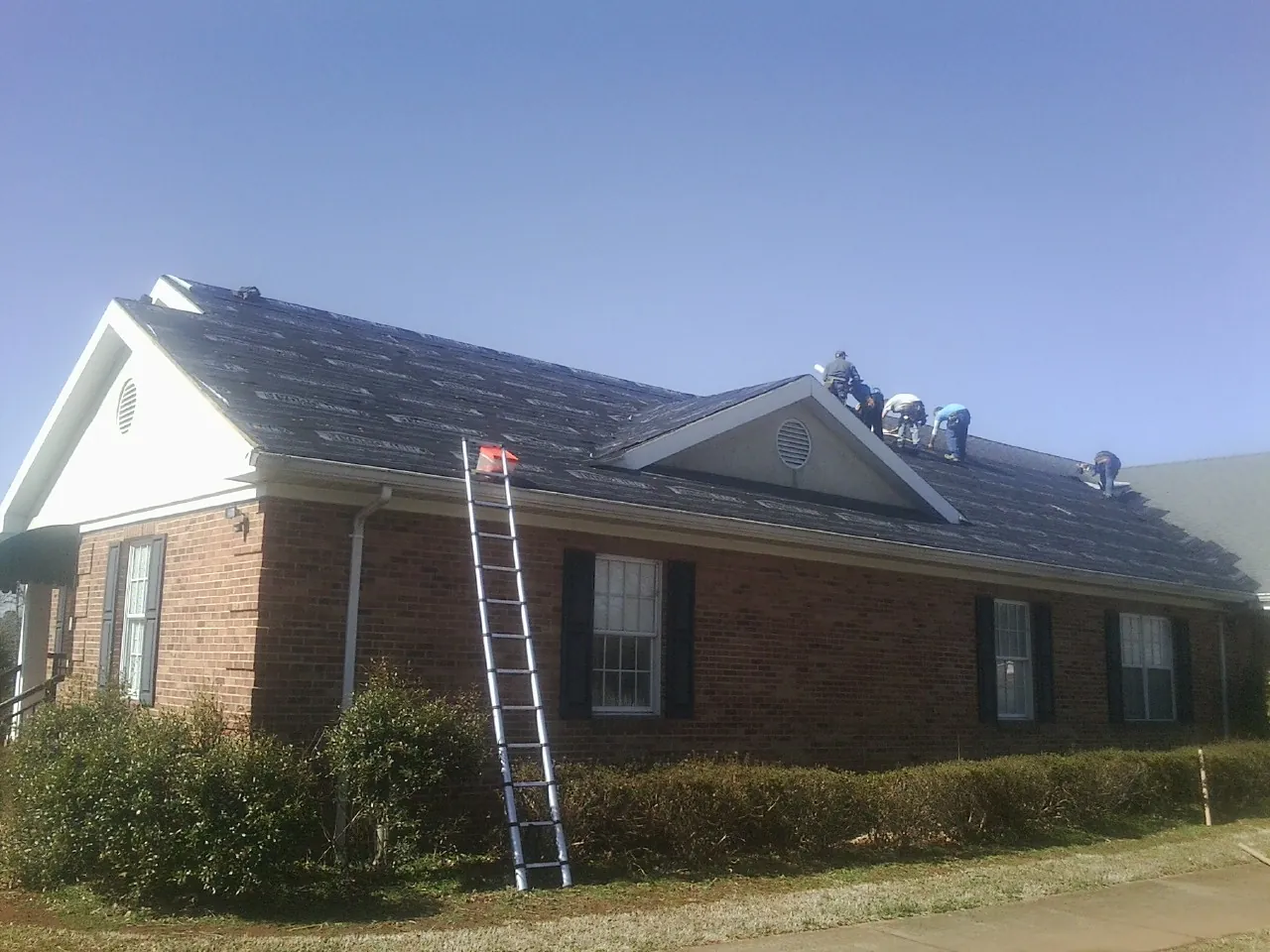 Crew tearing shingles off a brick ranch roof with a ladder set — Emergency Roof Repair work by our crew in East Hartford