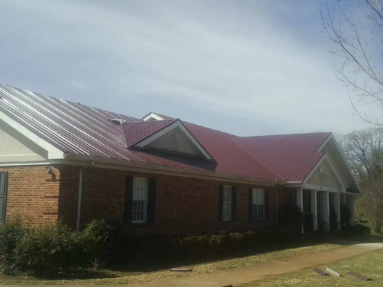 Red metal roof with gabled entries on a long brick building, from a Hail Damage Roof Repair job in East Hartford