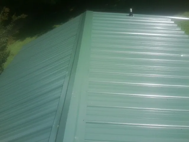 New green metal panels meeting at the ridge of a roof — Flat Roof Repair work by our crew in East Hartford