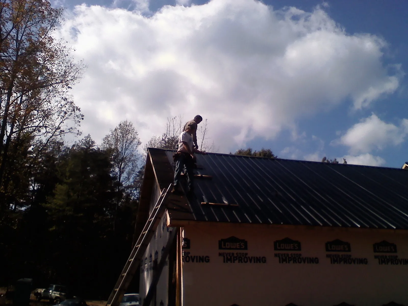 Roofer fastening dark metal panels high against a cloudy sky, from a Roof Inspection job in East Hartford