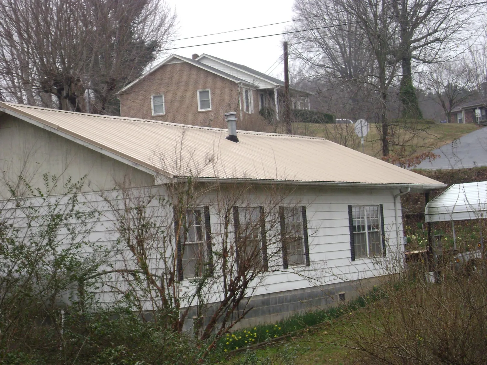 Tan metal roof on a white sided house set into a hillside — Commercial Roofing by Roofing Brothers in East Hartford